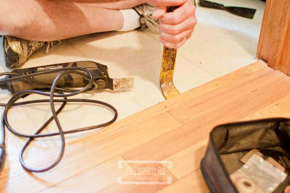 man using crowbar to remove baseboards for a cheap bathroom floor makeover