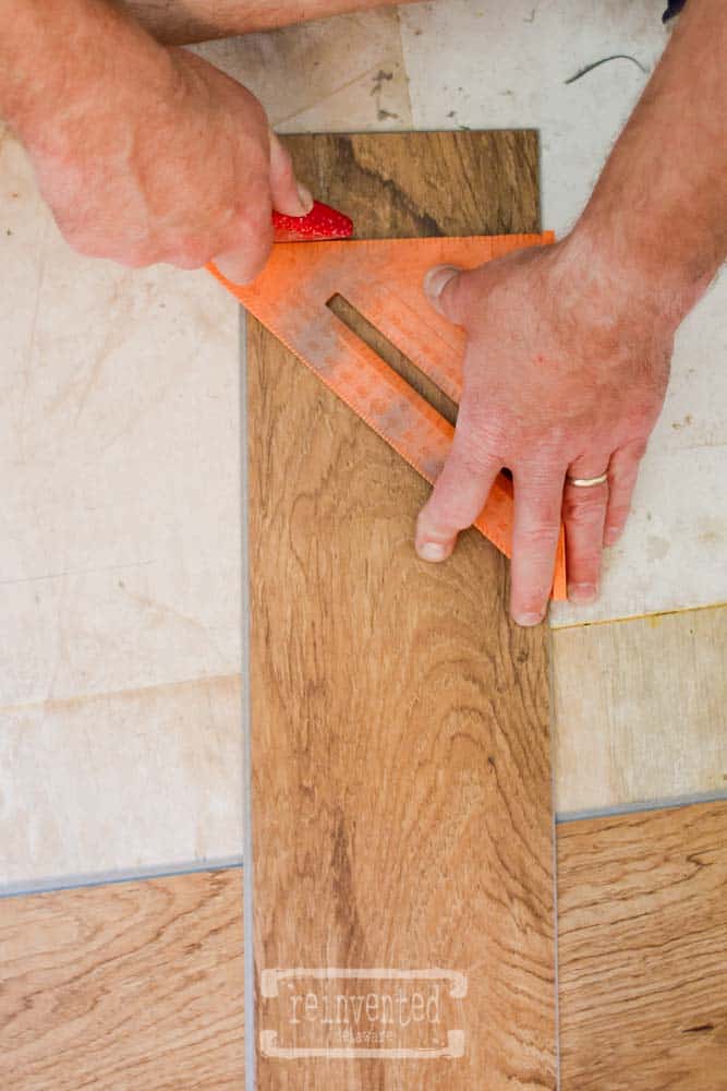 man using carpenters square to cut vinyl tiles in a bathroom remodel