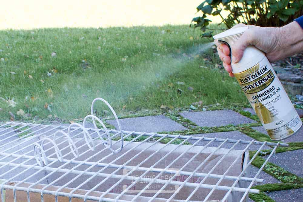 Lady spray painting a used box springs outside in the yard.