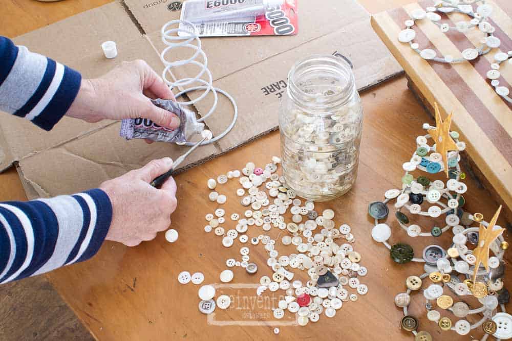 Lady gluing vintage buttons onto used bed springs to create a Christmas tree home decor piece.