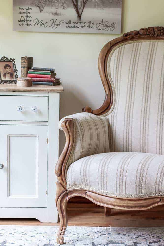 Victorian chair that has been reupholstered in reproduction grainsack fabric in neutral colors with a portion of a wahstand showing sitting next to the chair and staged with vinrtage books and a vintage picture