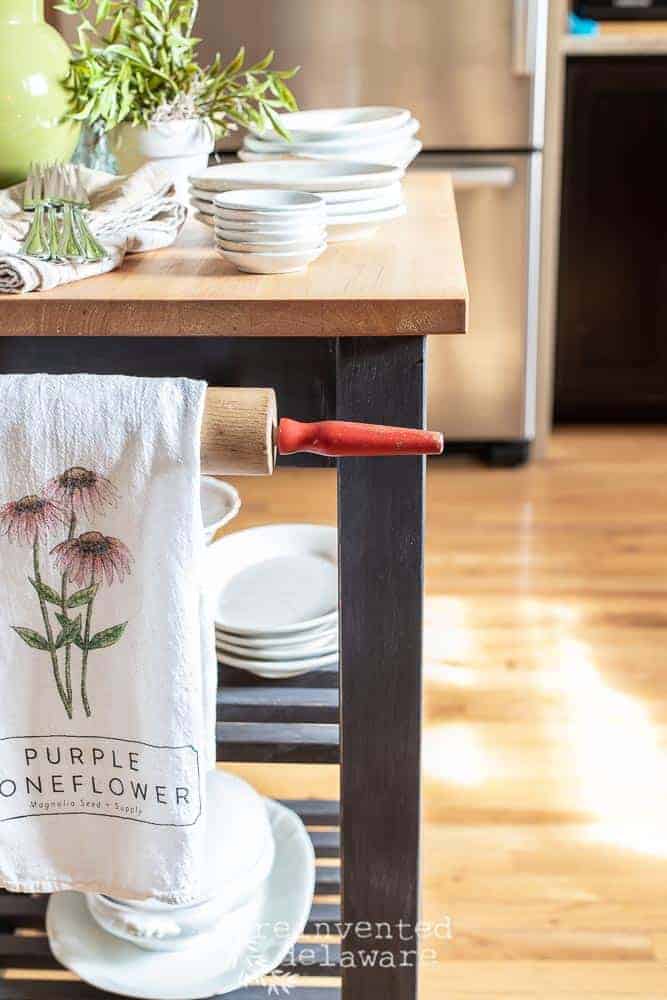 Close up view of repurposed rolling pin used as a towel holder on a repurposed rolling kitchen cart turned into a small kitchen island.