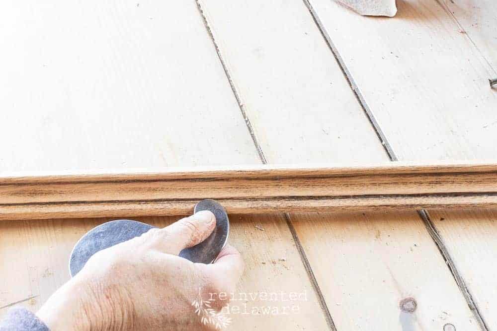 close up view showing the use of a scraper to remove old finish on antique furniture