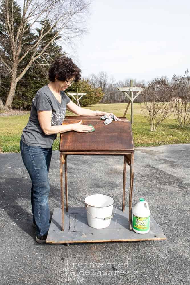 Lady scrubbing an antique fold down secretary desk for a tutorial on restoring old wood furniture.