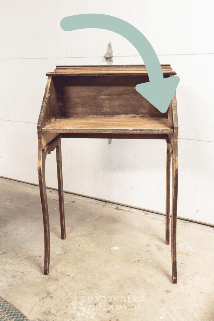 A fold down secretary desk with graphic arrow showing the repair that is needed to fix this old wood piece of furniture.