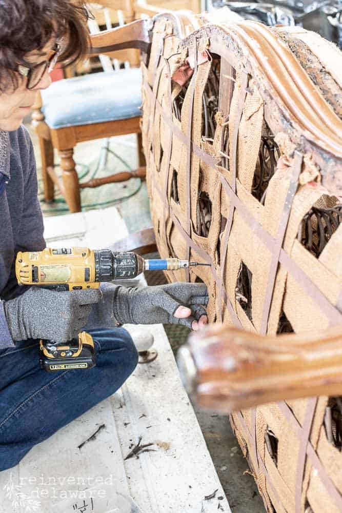 Lady using a power drill to repair the underside of an antique sofa.