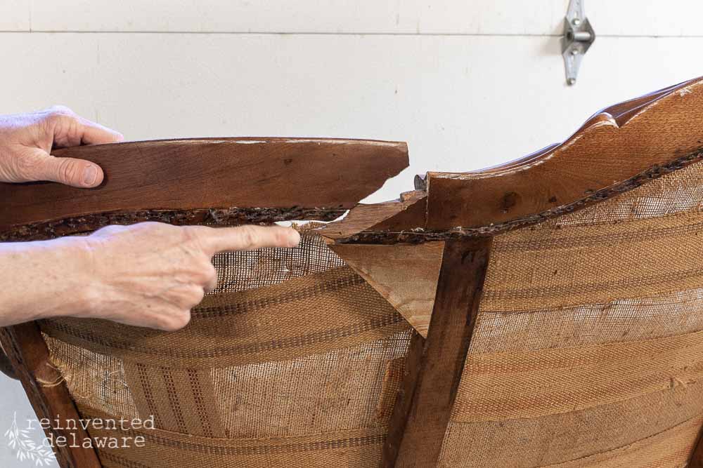 Lady pointing at the broken place on a wood frame of a Victorian antique couch.