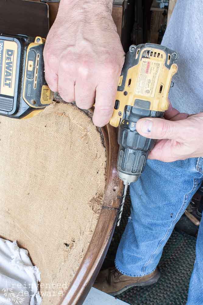 Man using a drill and drill bit to repair a damaged vintage settee.
