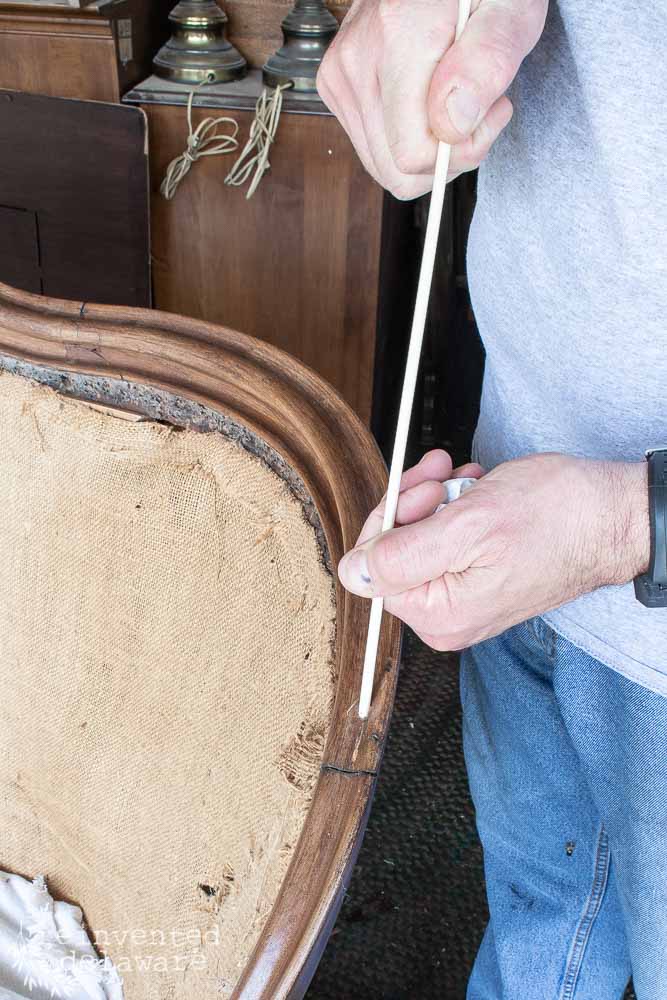 Man using a small dowel rod for a repair on a broken antique settee.