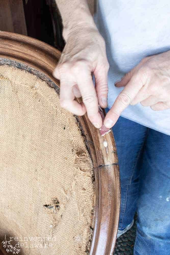 Close up view of woman sanding a small section of the wood frame on an anqiue victorian settee.