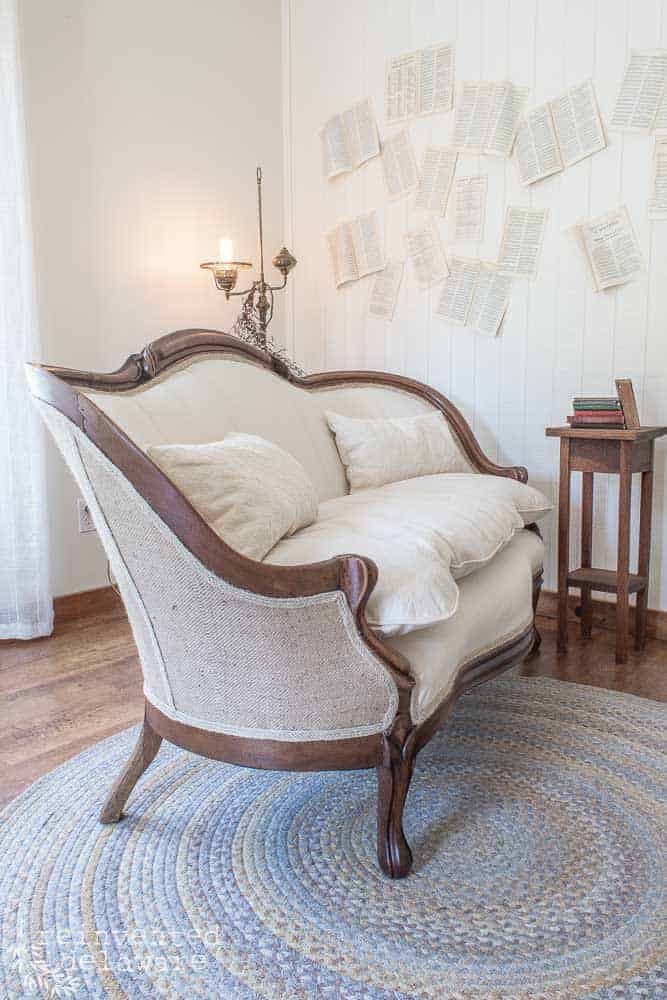 A staged antique sofa with a blue braided rug and book pages stuck on the wall in the background as wall decor.