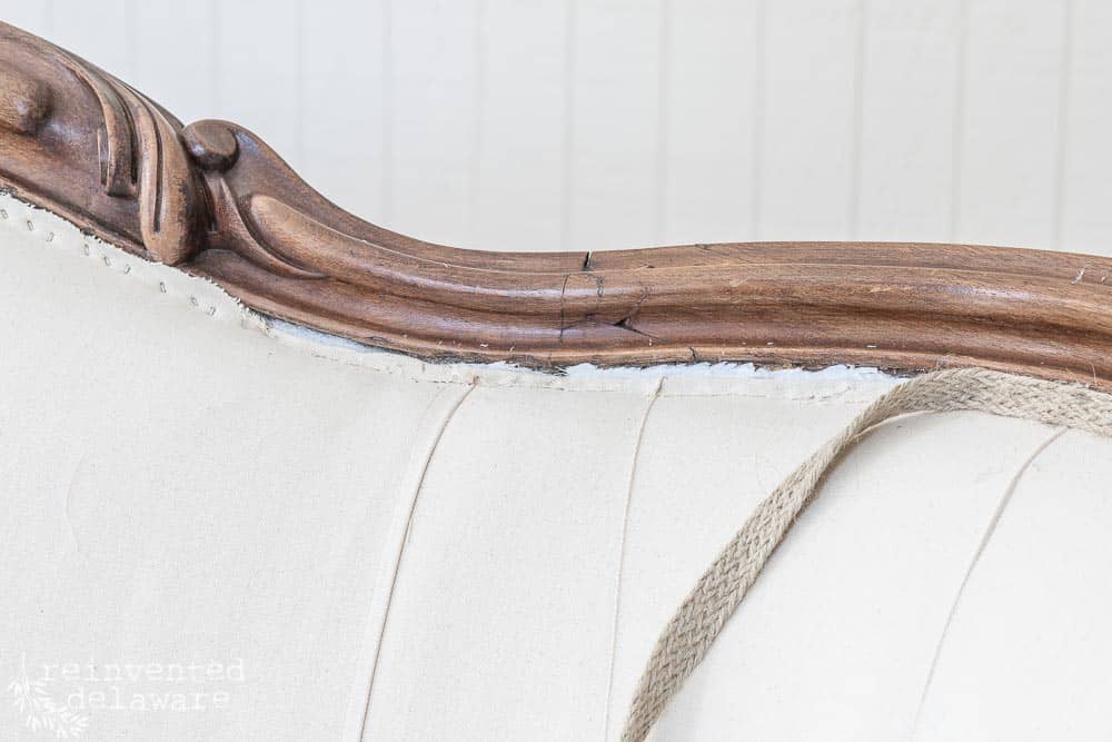 Close up view of jute trim being applied to cover stapled areas of upholstered sofa.