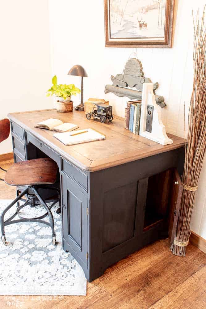 Top and side view of a hidden compartment in an old desk from the 1850s. Various desk items on the desktop and wall decor on the back wall behind the antique desk.