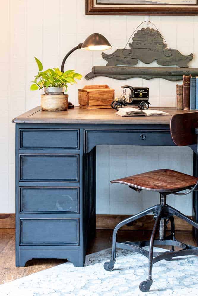 Left side of the antique desk with drawers that was painted in Miss Mustard Seed Milk Paint 'Typewriter' and also showing an antique desk chair on casters and various items on the desktop.