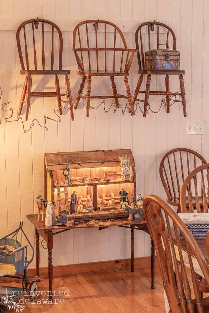 children's chairs hanging on a wall with bell garland hanging from chairs. nativity scene below chairs on a small vintage table