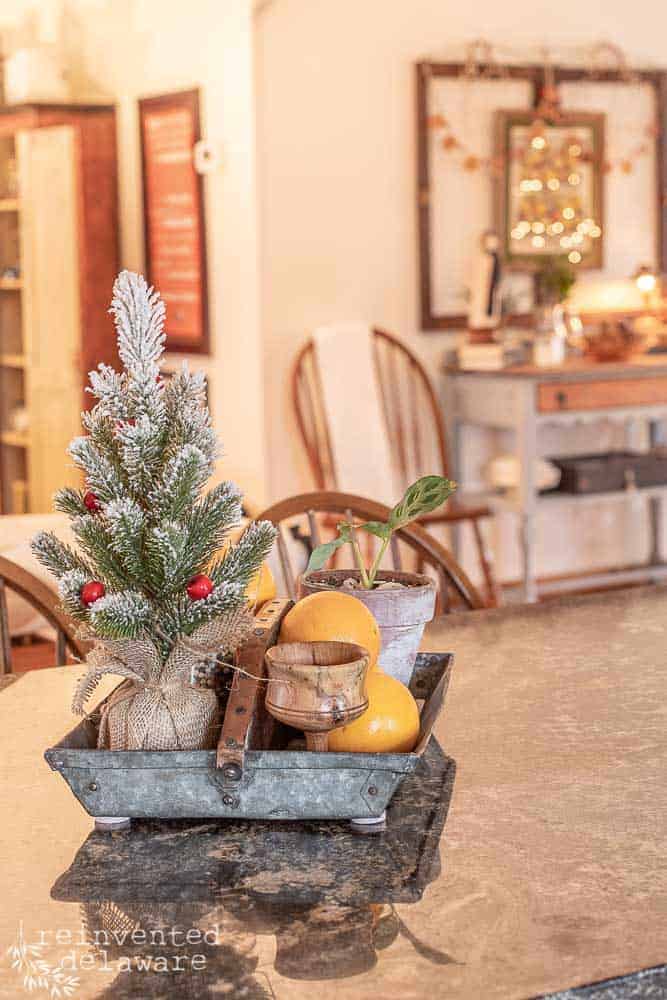 vintage metal tool caddy with small Christmas tree, several oranges, candle and salt & pepper shakers used as kitchen island centerpiece