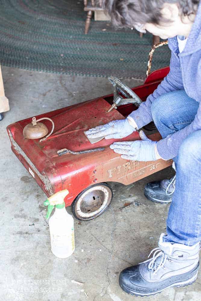 lady demonstrating how to clean rust off antique metal toy fire truck with vinegar and scrubbing