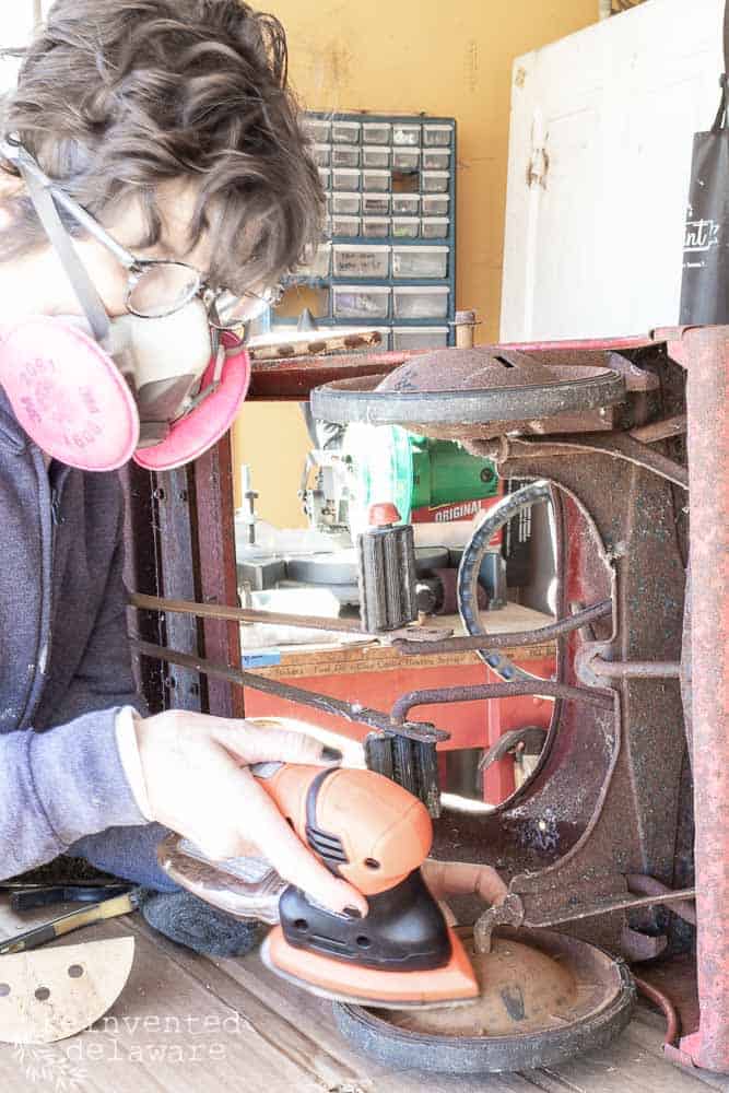 lady using mouse sander to clean rust off antique metal toy fire truck