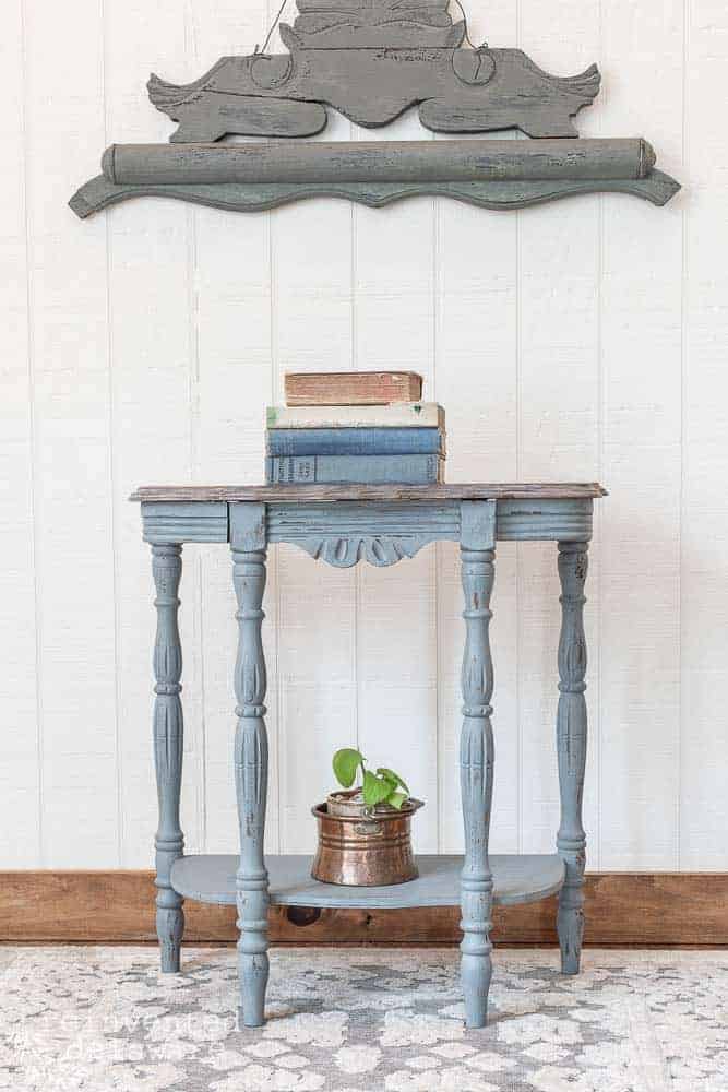 Demilune table with stack of books on top, plant on bottom shelf and wall decor