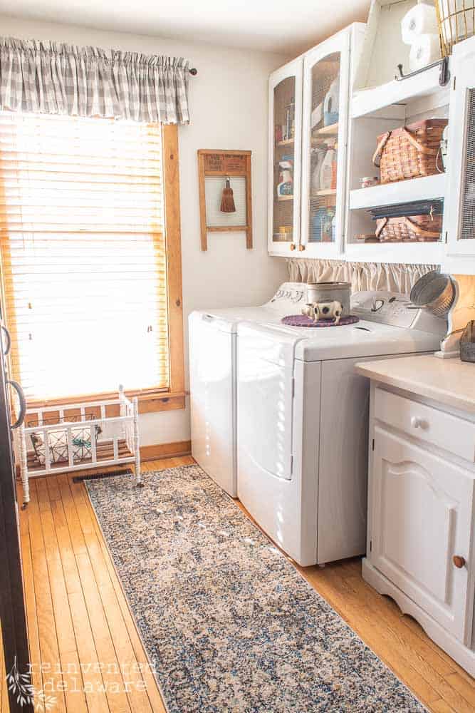 full view of laundry room that has been made over to be functional. washer, dryer, storage cabinet, shelving with baskets, new rug