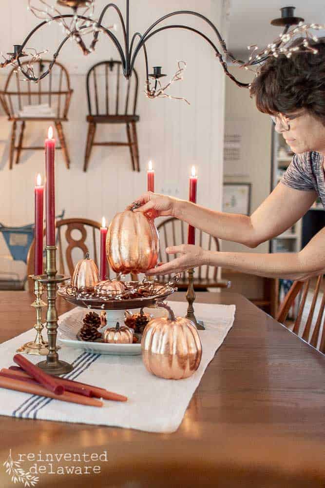 lady placing a copper leaf pumpkin on a dining table for fall decoration