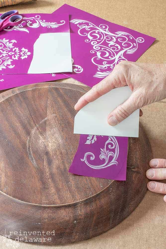 lady applying silk screen stencil to bottom of wooden cake plate