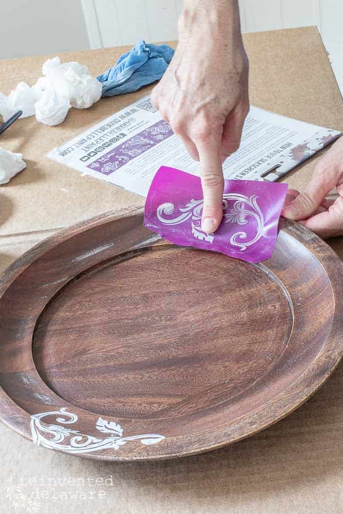 lady applying silkscreen stencil to wooden cake plate for thrift store home decor tutorial using a cake plate