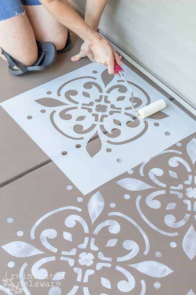 lady using paint foam roller and stencil to stencil the concrete front porch floor