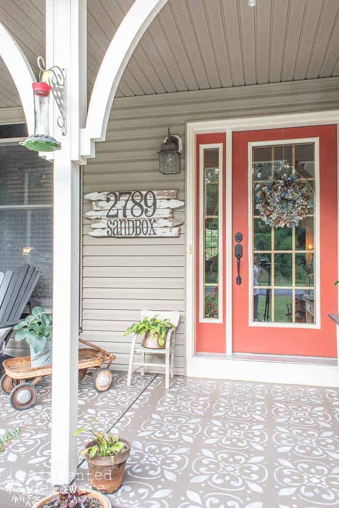 picture of red front door on a concrete front porch after makeover and showing various home decor and plants