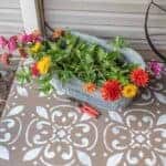 painted and stenciled concrete flool on front porch with a galvanized tub of cut zinnias