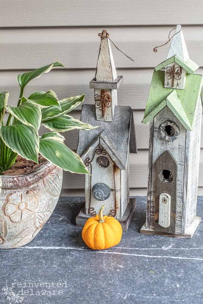 picture of home decor for a front porch with a small pumpkin sitting in front of two small church decor and a plant on the side
