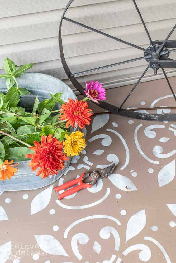 picture of a galvanzied tub filled with zinnia blooms and sitting on top of a painted and stenciled concrete front porch floor