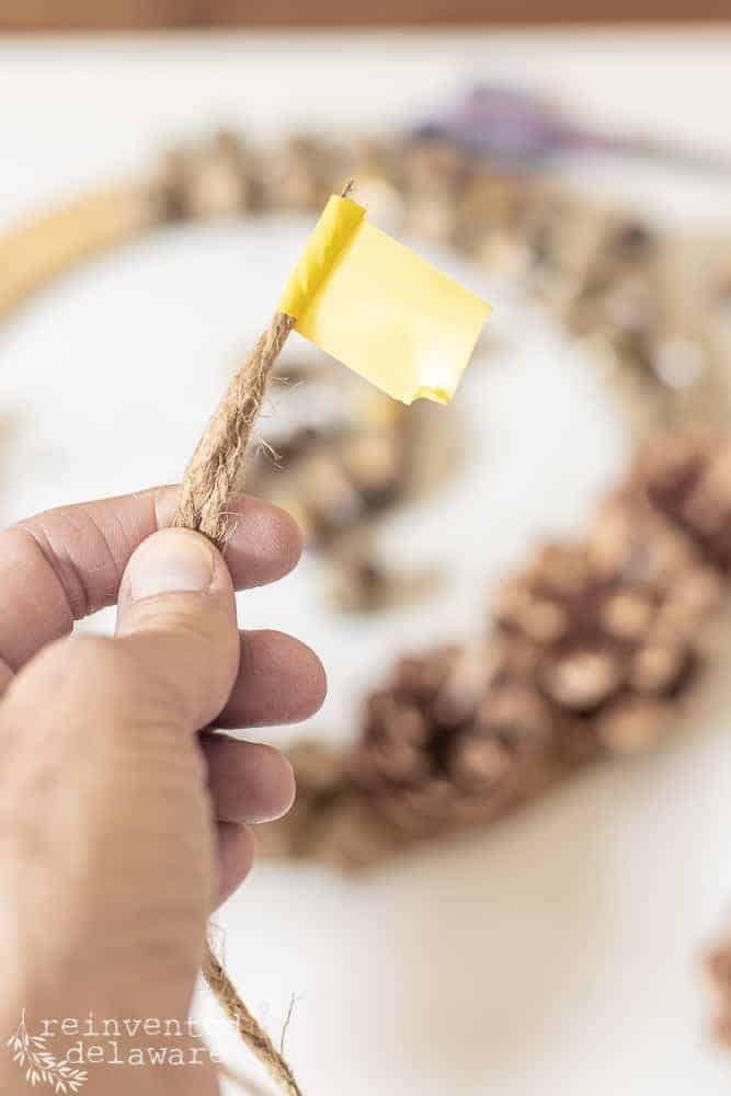 Lady showing close up of tape wrapped around the tip of the jute twine to prevent fraying and to make it easier to insert into the holes on the wood wreath form.