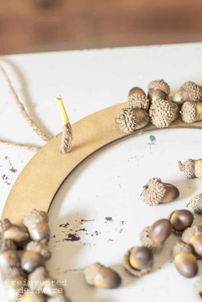 DIY pine cone wreath with acorns tutorial showing how to attach the jute twine hanger through one of the holes in the wood wreath form.