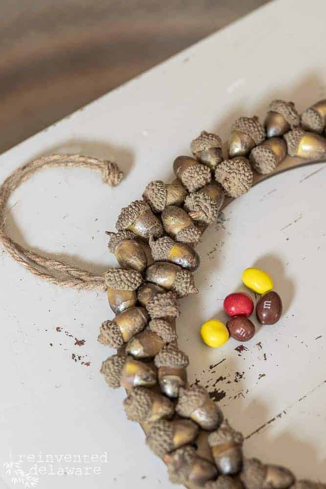 DIY pine cone wreath with acorns finished and sitting next to a pile of M&M candies.