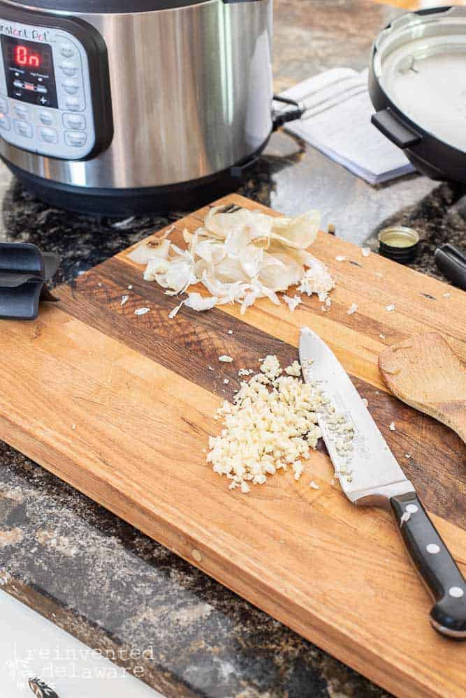 chopped garlic, garlic skins, chef's knife, cutting board on counter top with Instant Pot in background