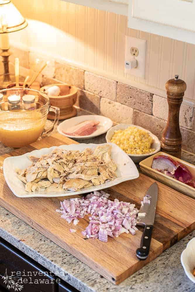 ingredients for chicken corn and butternut squash chowder sitting on a cutting board including cooked chicken, chopped onion, frozen corn and chicken stock