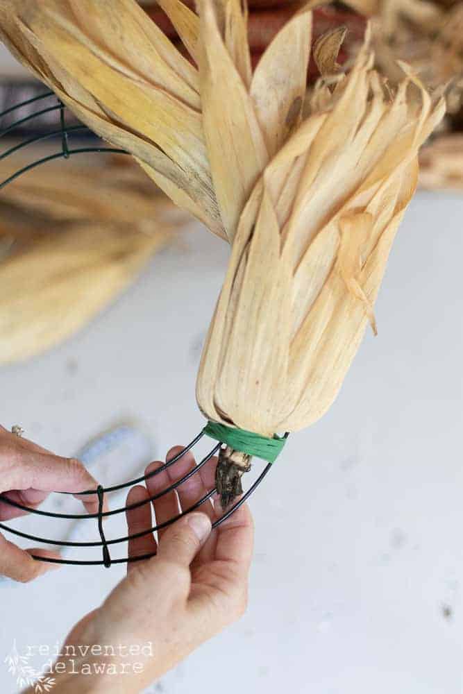 lady using floral tape to secure corn husk to wreath form