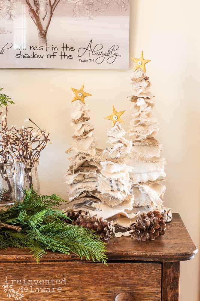 DIY Farmhouse Christmas trees staged on top of a dresser with fresh greenery and wall art in the background.