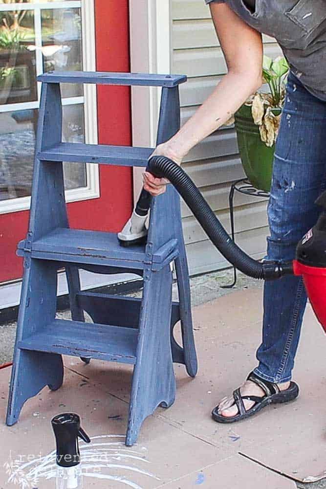 Lady using a shop vac to clean up flecks of paint leftover from chipping in the easy layered chippy paint finish tutorial.