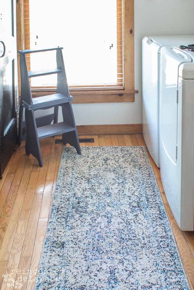 Flip foot stool/ladder with blue runner rug, washer and dryer, large window in a laundry room.