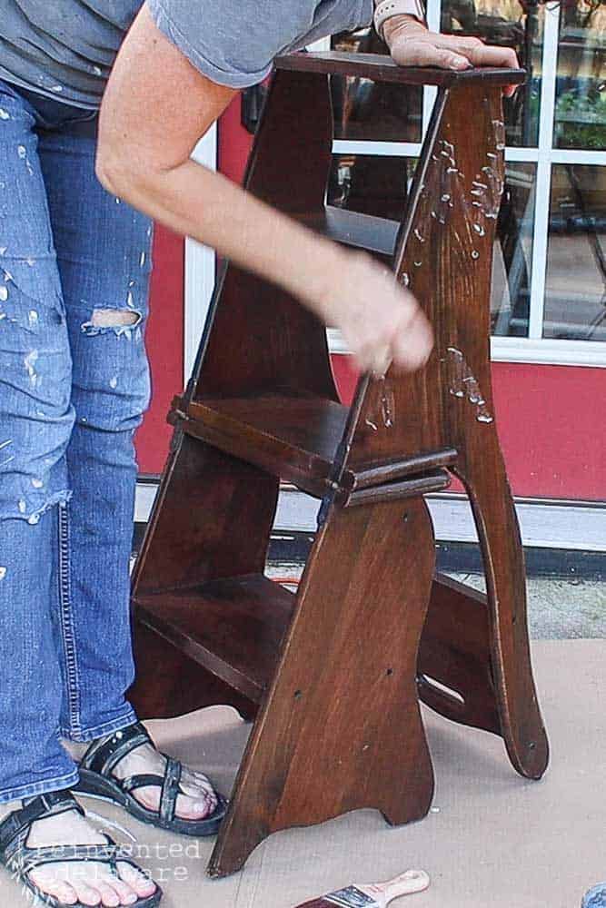 lady applying beeswax to a wooden step stool that is dark brown.