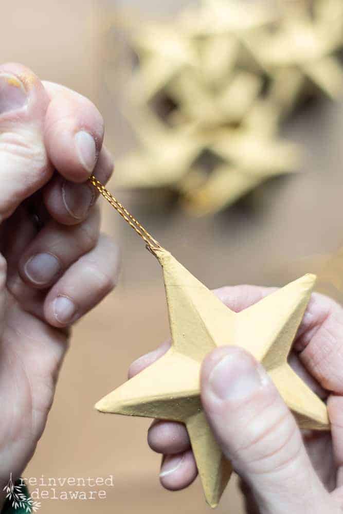 Lady removing gold string from paper mache star ornaments.