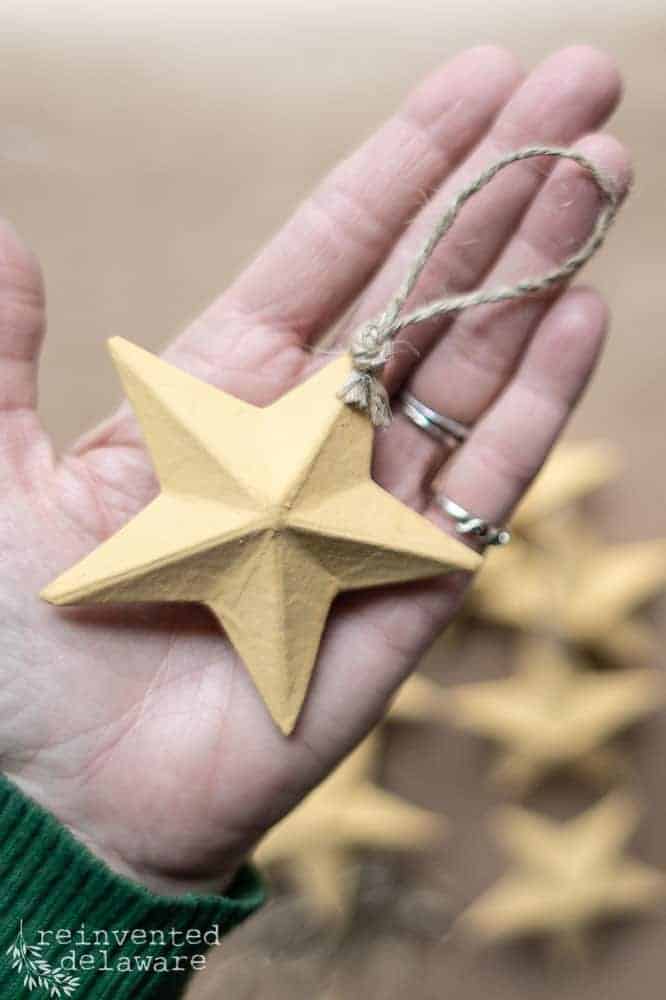 A lady's hand holding a painted paper mache star for a tutorial blog post about paper mache ideas.