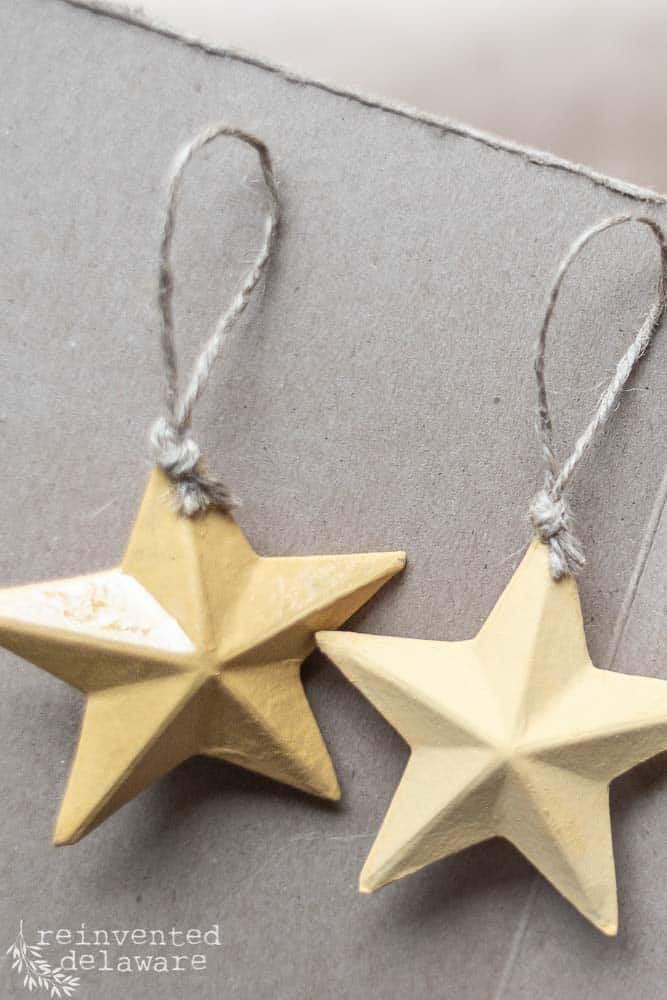 Two painted paper mache stars lying next to each other on a brown craft paper surface.
