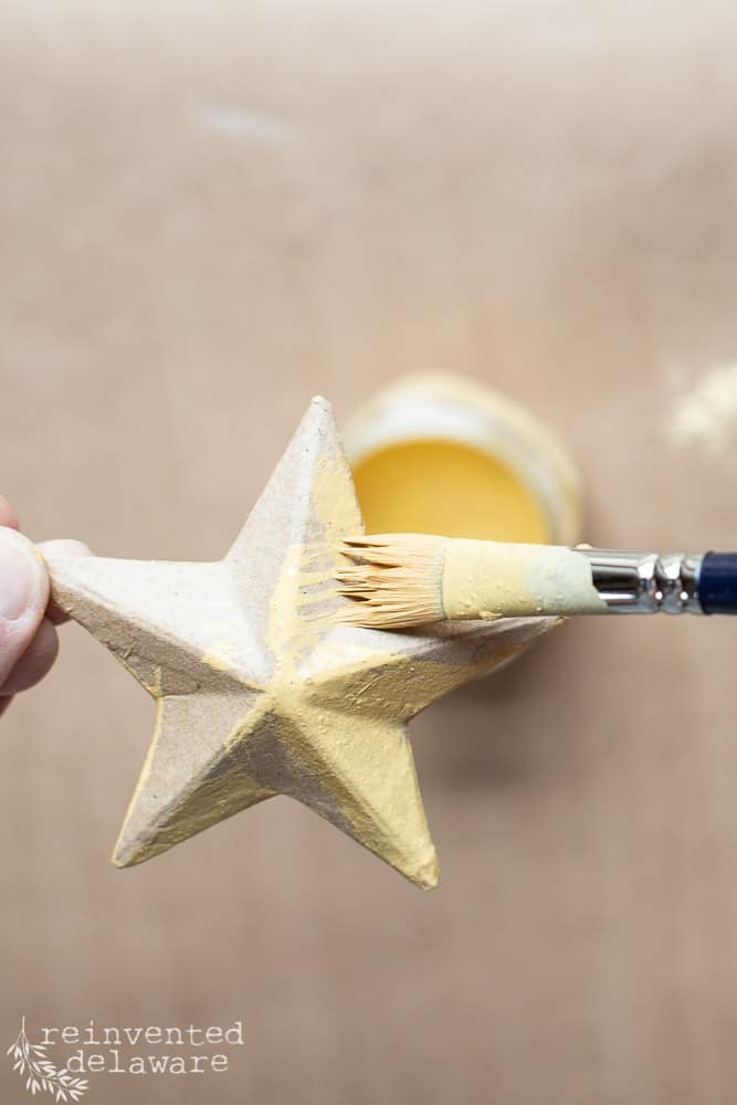 Paper mache star being painted in a yellow/gold color of milk paint.