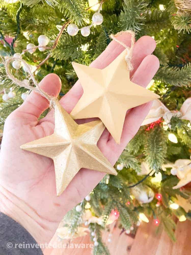 Close up view of painted paper mache stars being held by a ladies hand with a Chrismtas tree in the background.