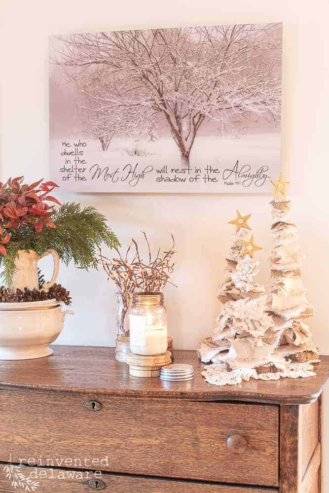 Antique dresser staged with handmade dropcloth Christmas trees, Antique Candle Co candle, irontstone dishes filled with Nandina clippings and pinecones and a piece of art work hanging on the wall.