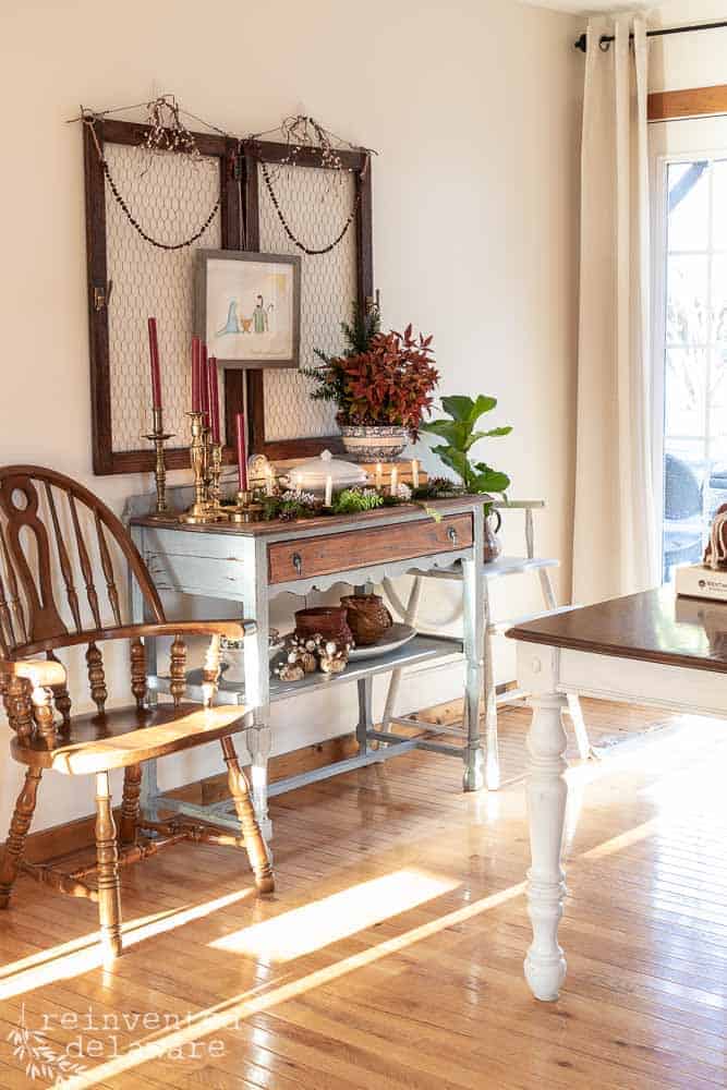 Scene of a dining area showing antique sideboard with various Christmas items sitting on the top including vintage Christmas candlesticks.
