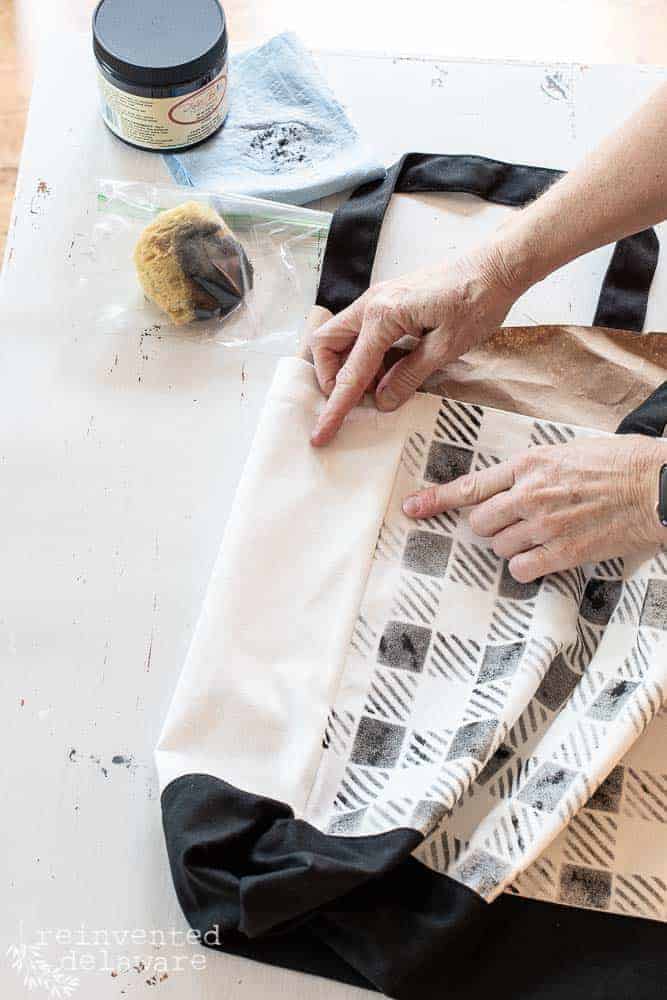 Lady pointing at side seam on a tote bag for placement of a fabric stencil.